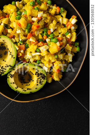 A hearty salad combines boiled egg, chicken breast, vibrant carrots, tender potatoes, green peas, and creamy avocado sprinkled with sesame seeds, all enhanced with olive oil 130568032