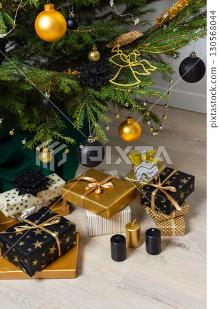 A festive scene featuring gold and black gift boxes, surrounded by shimmering candlelight and stylish decorations under a beautifully decorated Christmas tree, exuding elegance and charm 130568044