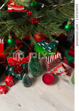 A festive display of green and red gift boxes under a beautifully decorated Christmas tree, complemented by candles and traditional ornaments, evoking warmth and holiday cheer A festive display of green and red gift boxes under a beautifully decorated Christmas tree, complemented by candles and traditional ornaments, evoking warmth and holiday cheer 130568045