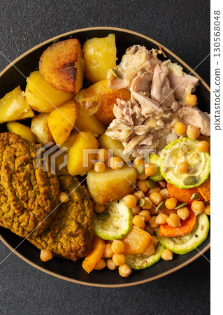 This hearty breakfast showcases a plate filled with baked sweet potatoes, carrots, zucchini, lentil cutlets, chicken breast 130568048