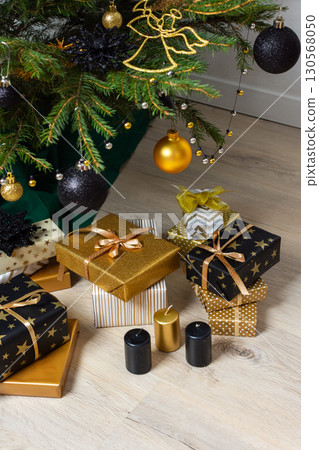 A festive scene featuring gold and black gift boxes, surrounded by shimmering candlelight and stylish decorations under a beautifully decorated Christmas tree, exuding elegance and charm A festive scene featuring gold and black gift boxes, surrounded by shimmering candlelight and stylish decorations under a beautifully decorated Christmas tree, exuding elegance and charm 130568050