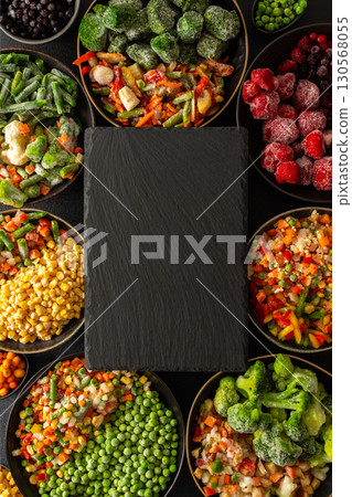 Fresh frozen vegetables and fruits arranged on a black ebonite board with a dark background, perfect for storing and preparing healthy, organic produce for the winter season 130568055
