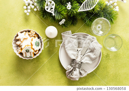 A top view of a Christmas table setting featuring an empty plate with napkin and cutlery, festive spruse and white tree decorations on a bright green background A top view of a Christmas table setting featuring an empty plate with napkin and cutlery, festive spruse and white tree decorations on a bright green background 130568058