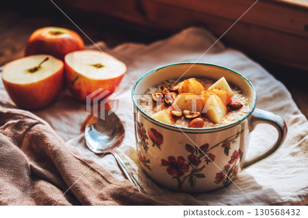 A cozy bowl of oatmeal sits on a rustic wooden table, adorned with fresh apple slices, chopped nuts, and a dash of cinnamon, capturing the essence of autumn breakfast delights 130568432