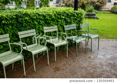 Wet green chairs standing at Royal library Garden in Copenhagen, Denmark. Famous park in city center in spring during the rain. Wet green chairs standing at Royal library Garden in Copenhagen, Denmark. Famous park in city center in spring during the rain. 130569463