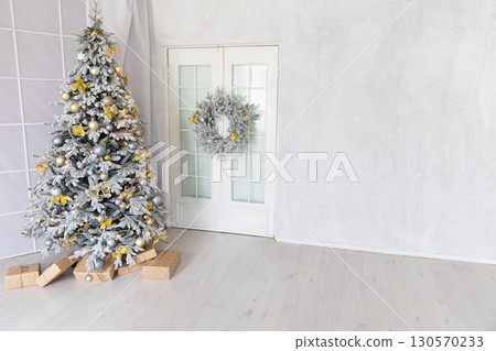 Christmas tree decorated with garlands and gifts in the interior of a white room for the new year Christmas tree decorated with garlands and gifts in the interior of a white room for the new year 130570233