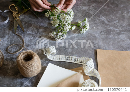 Creating a rustic floral arrangement with natural materials on a textured surface in a cozy crafting space 130570441