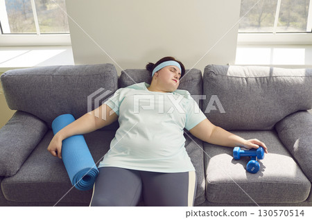 Fat tired after fit exercises woman wearing sportswear lying on sofa at home and having a rest. 130570514