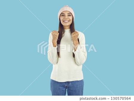 Overjoyed happy brunette girl in pink hat and white sweater showing yes gesture on blue background. 130570564
