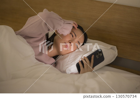 一名婦女在床上的看一個智能手機 130570734