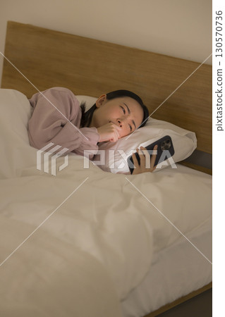 一名婦女在床上的看一個智能手機 130570736