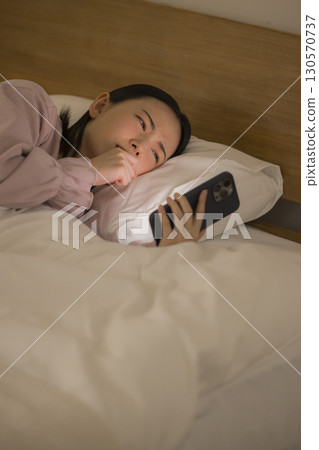 一名婦女在床上的看一個智能手機 130570737