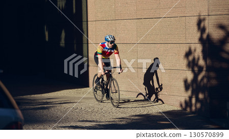 Cyclist riding road bike in shaded urban street with dramatic shadow on wall Cyclist riding road bike in shaded urban street with dramatic shadow on wall 130570899
