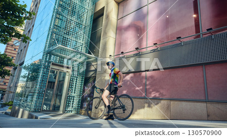 Cyclist resting with road bike near glass building in urban environment Cyclist resting with road bike near glass building in urban environment 130570900