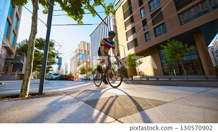 Cyclist riding road bike through urban street with modern buildings and sunlight Cyclist riding road bike through urban street with modern buildings and sunlight 130570902