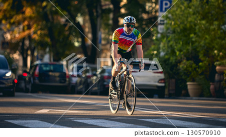 Cyclist in colorful jersey riding road bike on city street in sunset light 130570910
