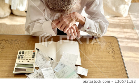 An elderly woman worried in front of a calculator and receipt _ front view 130571188