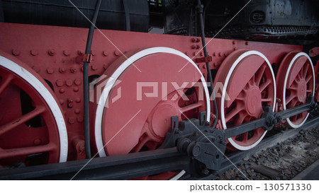 Bright red wheels of a vintage steam engine are prominently displayed at a railway museum. This showcases the intricate design and historical significance of rail travel. Bright red wheels of a vintage steam engine are prominently displayed at a railway museum. This showcases the intricate design and historical significance of rail travel. 130571330
