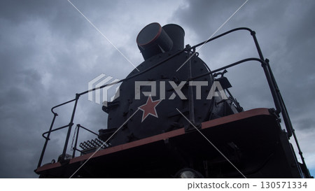 A vintage steam locomotive is prominently displayed against a backdrop of dark, ominous clouds. The structure features a striking red star, emphasizing its historical significance. 130571334