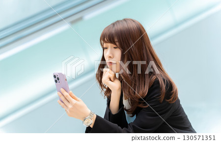 Woman/businesswoman thinking while looking at smartphone 130571351