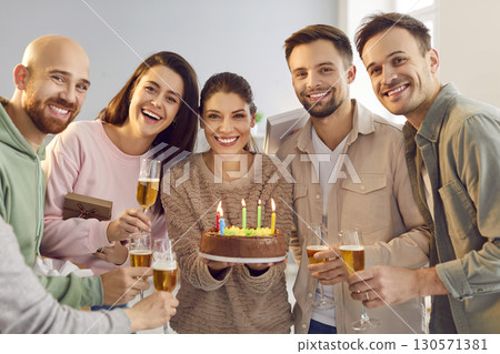 Happy woman holding birthday cake with friends holding glasses of champagne indoors. 130571381