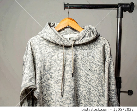 Gray Heathered Hoodie Hanging on Wooden Hanger with Clothes Rack Against Gray Background 130572022