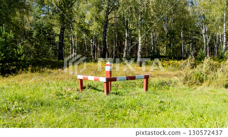 Red white striped boundary stake marking forest land limits in a grassy forest area, surrounded by vegetation. Ideal for surveying, property. Red white striped boundary stake marking forest land limits in a grassy forest area, surrounded by vegetation. Ideal for surveying, property. 130572437