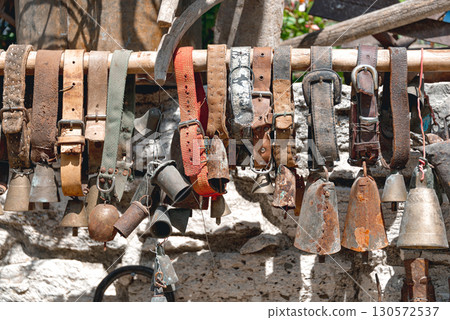 Traditional cypriot goat bell hanging from worn leather belts displayed on a wooden stick, showcasing traditional farm elements Traditional cypriot goat bell hanging from worn leather belts displayed on a wooden stick, showcasing traditional farm elements 130572537