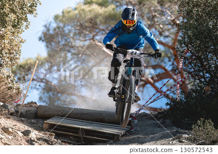Mountain biker jumping high, wearing protective gear during intense enduro race, navigating wooden ramp with professional skill 130572543