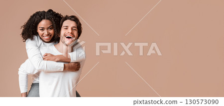 Piggyback ride. Affectionate guy carrying his black girlfriend on back, interracial couple bonding together over yellow background with free space 130573090