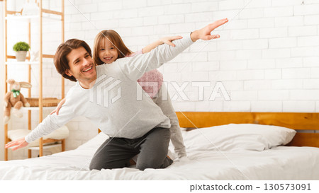 Young father and little daughter imitating airplanes, playing in bed in the morning, happy weekend together 130573091