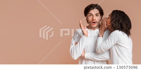 Hot Gossips. Black Girlfriend Whispering Secret To Her Shocked Boyfriend's Ear, Telling Something Surprising, Standing Together On Yellow Background 130573096