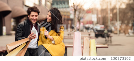 Happy shopaholics sitting on bench and shopping online with credit card and phone, panorama with copy space Happy shopaholics sitting on bench and shopping online with credit card and phone, panorama with copy space 130573102