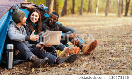Cheerful international friends sitting in tent, discussing route, using laptop, free space Cheerful international friends sitting in tent, discussing route, using laptop, free space 130573126