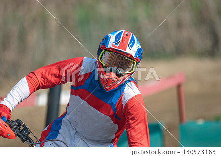 Motocross rider wearing helmet and goggles racing on dirt track 130573163