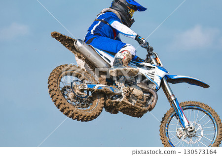 Motocross racer performing a high jump with blue sky background 130573164