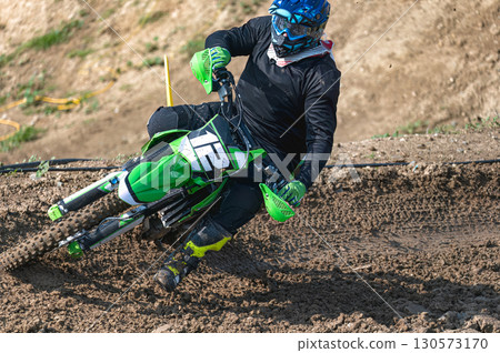 Motocross racer is leaning into a turn on a dirt track 130573170