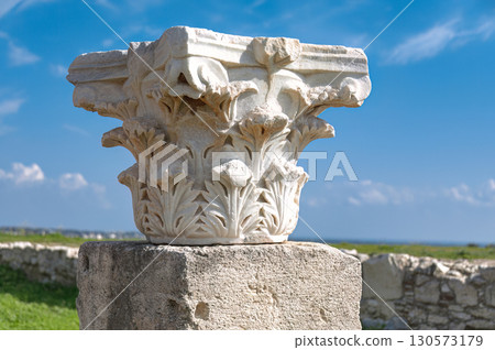 White marble corinthian capital with acanthus leaves decorations standing on a stone base at Kourion archaeological site, against blue sky. Cyprus 130573179