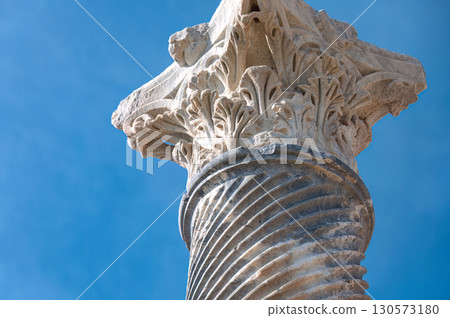 Weathered corinthian capital crowning limestone column, highlighting ancient architectural details against azure sky at Kourion archaeological site. Cyprus 130573180