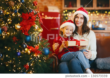Happy little girl holding desirable Christmas gift, celebrating xmas with parents at home 130573339