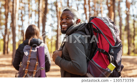 Happy black guy with backpack looking aside, hiking with girlfriend at forest 130573359