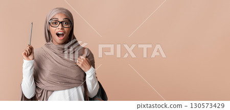 Muslim Nerd. Funny inspired black islamic girl in hijab and eyeglasses raising pencil up, having idea, posing over yellow background, free space Muslim Nerd. Funny inspired black islamic girl in hijab and eyeglasses raising pencil up, having idea, posing over yellow background, free space 130573429
