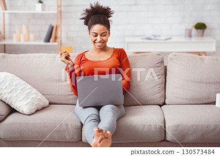Online Shopping. Smiling Afro Woman With Laptop And Credit Card Buying Things On Internet Sitting On Sofa At Home Online Shopping. Smiling Afro Woman With Laptop And Credit Card Buying Things On Internet Sitting On Sofa At Home 130573484