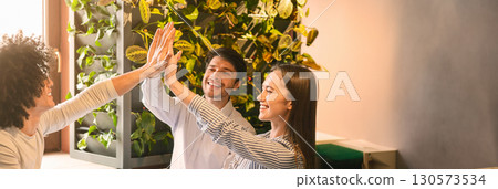 Excited multiethnic team giving each other high five, celebrating success while working together on project at cafe, copy space 130573534