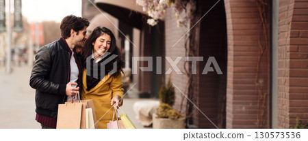 A happy couple strolls through a vibrant outdoor market, holding shopping bags while smiling and enjoying each other's company, copy space A happy couple strolls through a vibrant outdoor market, holding shopping bags while smiling and enjoying each other's company, copy space 130573536