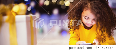 Cute little african girl playing with cell phone at Christmas eve, free space Cute little african girl playing with cell phone at Christmas eve, free space 130573752