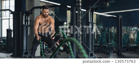Fitness man working out with battle ropes at gym interior, free space, web-banner 130573763