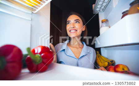 Cheerful young woman taking vegetables in fridge for preparing lunch , view from inside Cheerful young woman taking vegetables in fridge for preparing lunch , view from inside 130573802