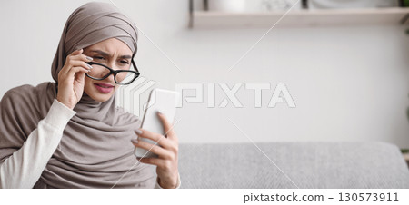 Young arabic girl in hijab with poor eyesight vision looking at cellphone screen through glasses, trying to read message, free space Young arabic girl in hijab with poor eyesight vision looking at cellphone screen through glasses, trying to read message, free space 130573911