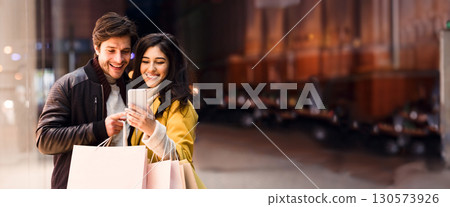 Happy couple ordering taxi on cellphone, walking near city center after shopping on weekend, copy space Happy couple ordering taxi on cellphone, walking near city center after shopping on weekend, copy space 130573926